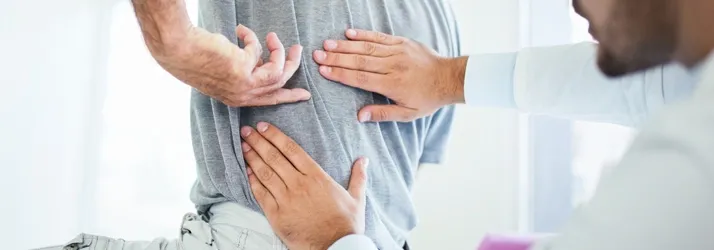 Hands positioned on a person’s lower back while another hand points to the same area.