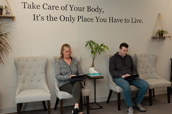 Two people seated in a waiting room using tablets beneath a wall quote and decorative plants.