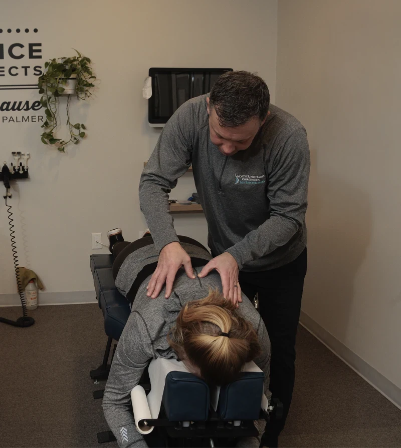 Chiropractor performing a spinal adjustment on a patient lying face down on a treatment table.